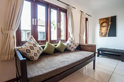 a couch with pillows sitting in a room with windows at Villa Annecy in Seminyak