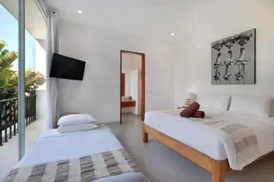 two beds in a white room with a tv at Villa Indaros in Seminyak