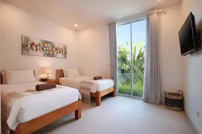 a bedroom with two beds and a large window at Villa Indaros in Seminyak