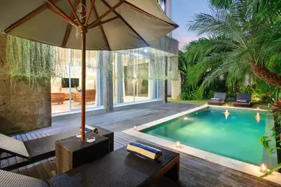 a swimming pool with a table and an umbrella at Villa Indaros in Seminyak