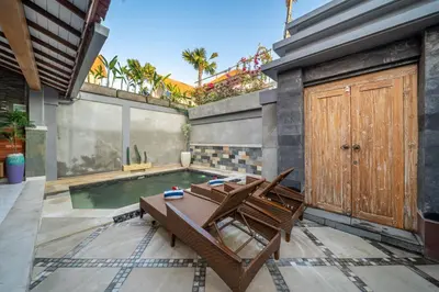 a patio with a pool and two chairs in front of a house at Q LA Villas in Seminyak