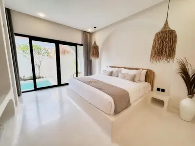 a white bedroom with a large bed and large windows at Armonia Bali Legian Villas in Legian