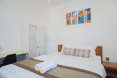 a bedroom with a large white bed and a desk at Fun Living Guest House in Seminyak