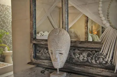 a wooden head statue in front of a bed at Frangipani Villa Seminyak - 2BR Pool Walk to Beach in Seminyak