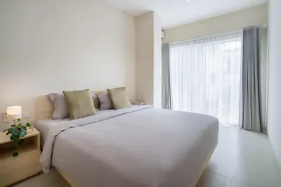 a white bedroom with a large bed and a large window at Bali Bustle Sunset Coliving and Coworking Space in Legian