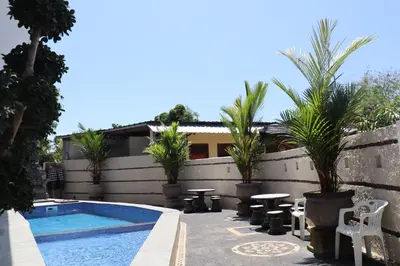 a swimming pool with a table and chairs and palm trees at Kubu Celagi Manis in Jimbaran