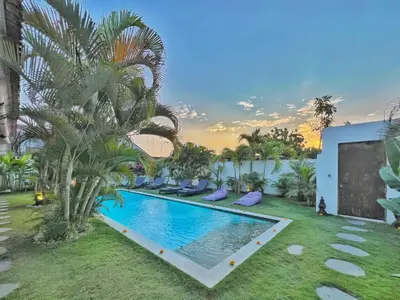 a swimming pool in a yard with palm trees at Villa Rocher - Modern 3 BR Villa Batu Belig 3 min beach in Seminyak