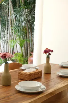 a wooden table with white plates and flowers in vases at Uma dharma villas in Seminyak