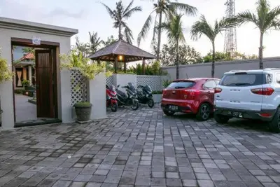 two cars and motorcycles parked in a parking lot at arimanu rooms in Kuta