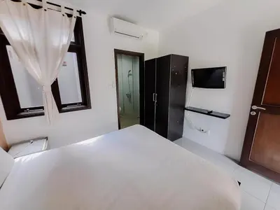 a bedroom with a large white bed and a television at arimanu rooms in Kuta