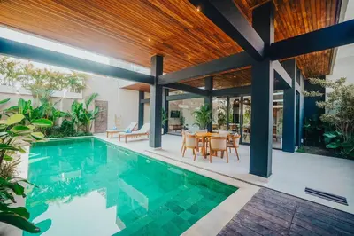 an indoor swimming pool with a dining area and a house at Villa Cintamu - Modern Spacious Villa in Prime Berawa Location in Canggu