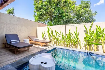 a swimming pool with a bench and a chair next to a fence at Rumah Kodel in Legian in Seminyak