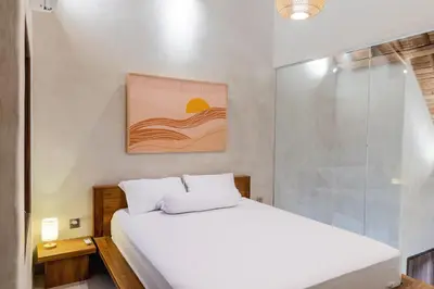 a bedroom with a white bed and a glass shower at Green Loft Citarum in Sanur