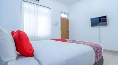 a white bed with red pillows in a bedroom at OYO 1755 De'balcon Accomodation Near Ngurah Rai Airport in Ngurah Rai International Airport