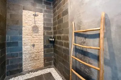 a bathroom with a shower with a stone wall at Vajrayana - 10 Min From The Beach, Serene Villa with Pool View in Kerobokan