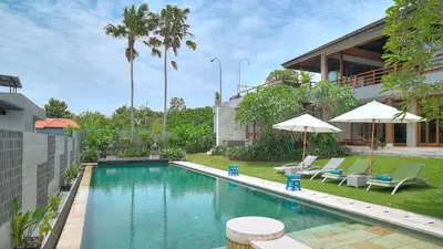 a swimming pool with chairs and umbrellas next to a house at Villa Aiko in Jimbaran