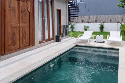 a swimming pool with two white chairs next to a house at Wakajima House Kerobokan by The Lavana in Kerobokan