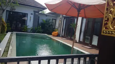 an umbrella next to a swimming pool with a house at Kubu Nesa in Jimbaran