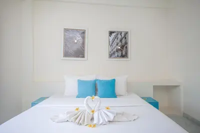 a white bed with blue pillows and a flower on it at Paras Paros Marina Lodge in Sanur