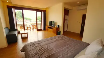 a bedroom with a bed and a chair and a balcony at BAGUS Guest House in Legian