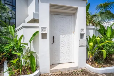 a white door in a white house with plants at Athos Villa by iBali Management in Seminyak