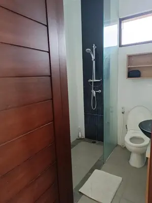 a bathroom with a toilet and a glass shower door at Casa Dijaweqo in Jimbaran