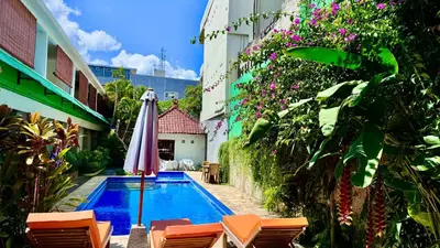 a pool with chairs and an umbrella next to a building at Ellenbrook Rooms 17 by Mulia Cottage in Seminyak