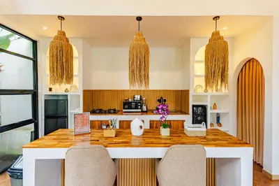 a kitchen with a counter with chairs and two chandeliers at Mya Harmony Villas Seminyak in Seminyak