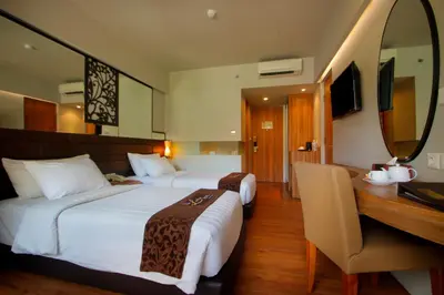 a hotel room with two beds and a desk and a mirror at The Lerina Hotel Nusa Dua in Nusa Dua