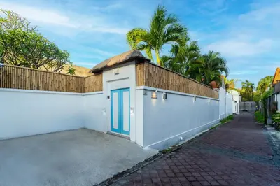 a white building with a blue door and a fence at Villa Bardo by Pertama Management in Seminyak