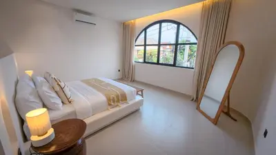 a white bedroom with a bed and a window at Miko Villa Seminyak in Seminyak
