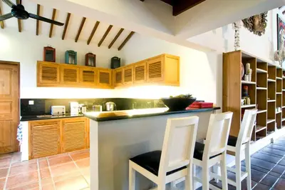 a kitchen with wooden cabinets and white bar stools at Villa Kija in Seminyak