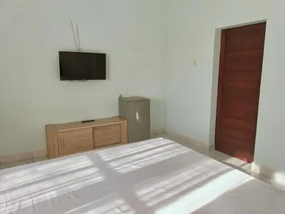 a bedroom with a bed and a dresser and a television at Bcoss Stay in Jimbaran