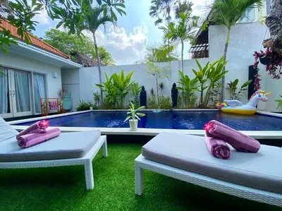 two beds with pink pillows in front of a swimming pool at Tranquil Family Villa Retreat in Umalas in Kerobokan