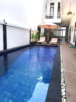a large swimming pool with chairs and an umbrella at Double D Guesthouse and Villa in Kerobokan