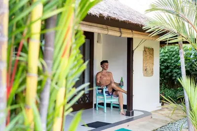 a man sitting on a chair on the porch of a house at Villa Nyumpene in Legian in Legian