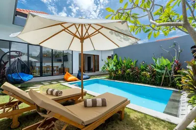 an umbrella and chairs next to a swimming pool at Ageta Villa 3 bedrooms Umalas with pool in Kerobokan