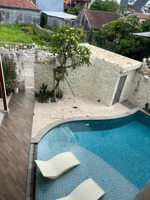 a swimming pool with two white chairs next to a building at HŌM Coliving Bali in Kerobokan