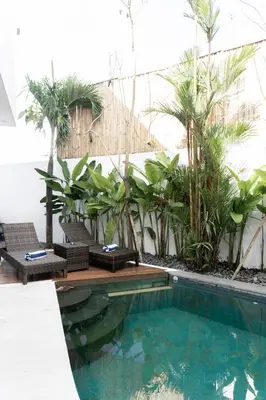 a swimming pool with chairs and palm trees in a building at Casa Luna Villa in Kerobokan