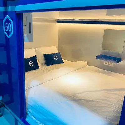 two twin beds in a room with a television at Rosalyne Sleepbox Denpasar Bali in Seminyak