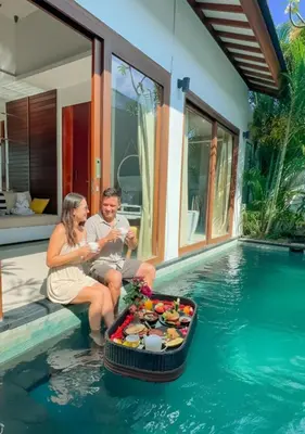 a man and woman sitting next to a tray of food in a pool at Anari Villas Kuta by The Wina Resorts in Legian