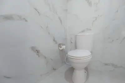 a white toilet in a bathroom with marble walls at Cherish Villa Umalas in Canggu