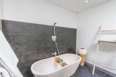 a bathroom with a white tub and a gray wall at Villa Alopa Seminyak in Seminyak