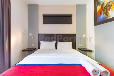 a bedroom with a white bed with a red blanket at Ozz Hotel Kuta Bali manage by Ozz Group in Kuta