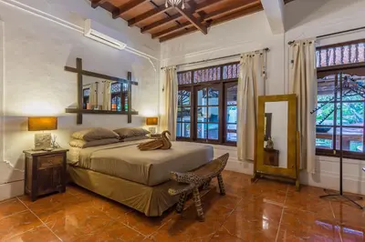 a bedroom with a bed and a chair and windows at Villa Blue - 4BR authentic and atypical villa in Seminyak in Seminyak