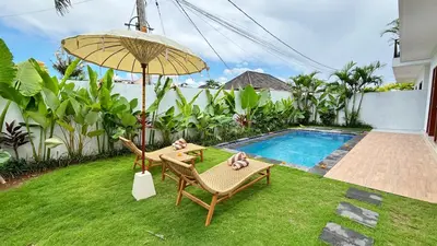 a yard with two chairs and an umbrella and a pool at Villa Bumbabu in Kerobokan