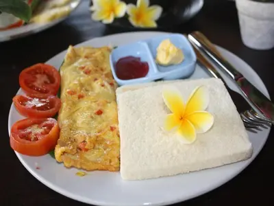 a plate of breakfast food with a omelet and tomatoes at D'Mell Bali in Nusa Dua