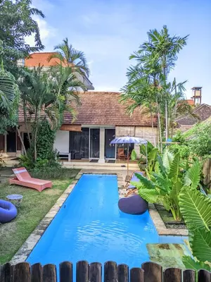 a pool in the backyard of a house with palm trees at Two Brothers Guesthouse in Legian
