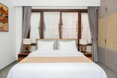 a bedroom with a large white bed and windows at The Mango Villa Jimbaran Jimbaran in Jimbaran