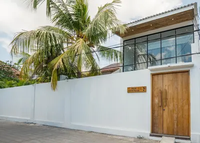 a white building with a wooden door and a palm tree at Villa Casa Goya - Lofty Pool Villa Near The Beach in Vibrant Legian in Legian